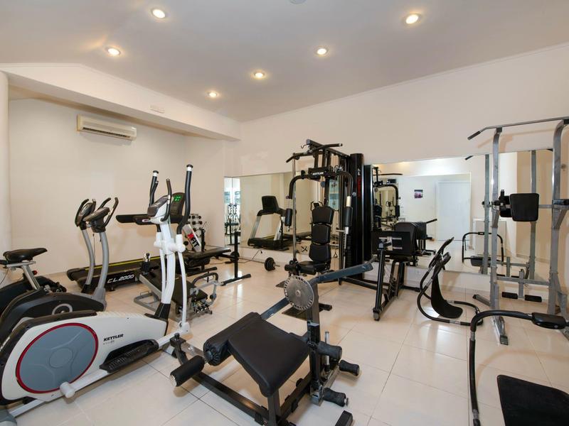 Moderní posilovna s rotopedy, posilovacími stroji a lavičkami v světlé místnosti.