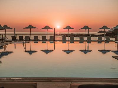 Pool mit Liegestühlen und Sonnenschirmen bei Sonnenuntergang am Meer.