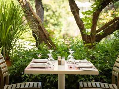 Ein gedeckter Tisch für vier Personen in einem grünen Gartenbereich eines Hotels.