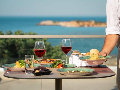 Kelner niosący tacę z napojami i jedzeniem na tarasie z widokiem na morze.