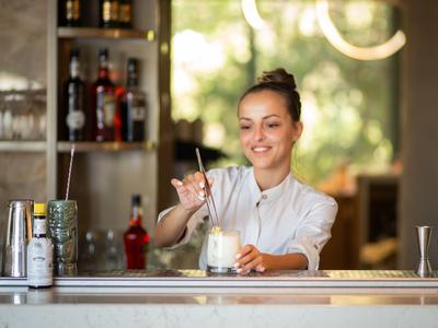 Lächelnde Barkeeperin bereitet an einer Bar einen Cocktail mit Schlagsahne zu.