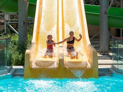 Zwei Kinder rutschen nebeneinander eine gelbe Wasserrutsche ins Schwimmbecken hinunter.