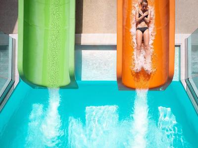 Frau rutscht eine orangerutsche in einen Pool mit einer grünen Rutsche daneben.