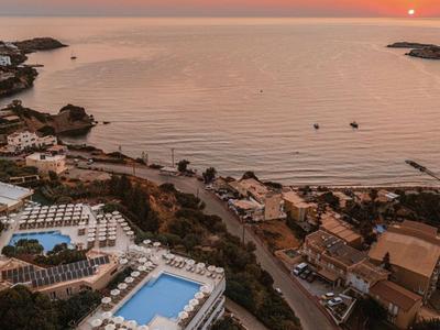 Widok z lotu ptaka na nadmorskie miasto z hotelami, basenami i zachodem słońca nad morzem.