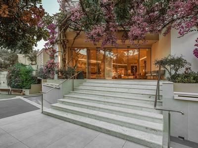 Wejście do hotelu z szerokimi schodami i kwitnącymi roślinami nad nimi.