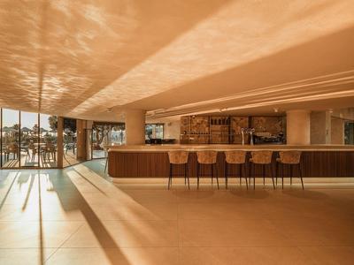 Nowoczesny bar hotelowy z drewnianym kontuar, hokerami i dużymi oknami z promieniami słonecznymi.