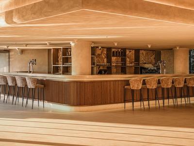 Moderner Hotelbarbereich mit Holztheke und Barhockern in warmen Tönen.