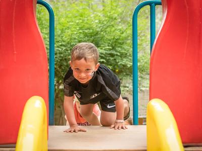 Szczęśliwy chłopiec wspina się po placu zabaw z zielonym otoczeniem.