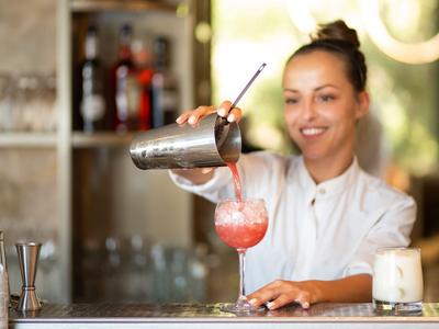 Barmanka nalewa różowy koktajl do szklanki przy barze