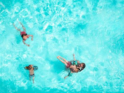 Trzy osoby pływają swobodnie w czystym turkusowym basenie.