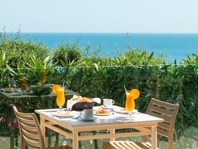 Stół ze śniadaniem na tarasie z widokiem na morze i zielone rośliny.