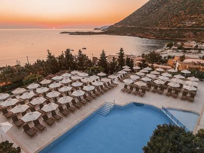 Zachód słońca nad kurortem z basenem i leżakami przy morzu.