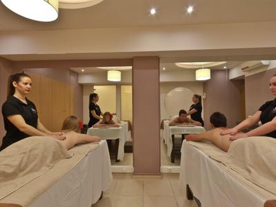 Zwei Frauen massieren Männer in einem ruhigen Spa-Raum mit warmem Licht.