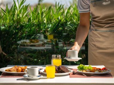 Osoba podaje kawę przy stole z śniadaniem, sokiem i różnymi daniami na zewnątrz.