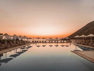 Spokojny basen o zachodzie słońca z leżakami i parasolami na krawędzi.