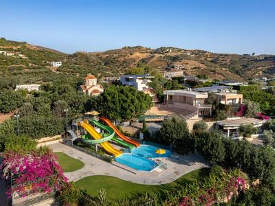 Freizeitpark mit Wasserrutschen und Schwimmbecken, umgeben von grünen Hügeln und Gebäuden.