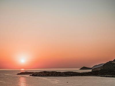 Zachód słońca nad spokojnym morzem z skalistym wybrzeżem i wzgórzami po prawej stronie