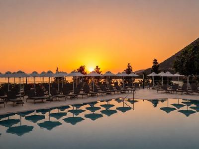 Sonnenuntergang über einem Hotelpool mit Sonnenschirmen und Liegen am Meer.