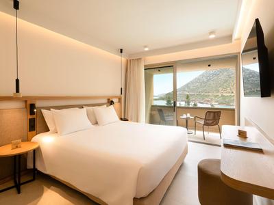 Modernes Hotelzimmer mit großem Bett, Balkon mit Bergblick und heller, schlichter Einrichtung.