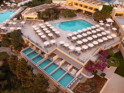 Luxushotel mit mehreren Pools, Sonnenliegen und umliegender Natur in einem mediterranen Stil.