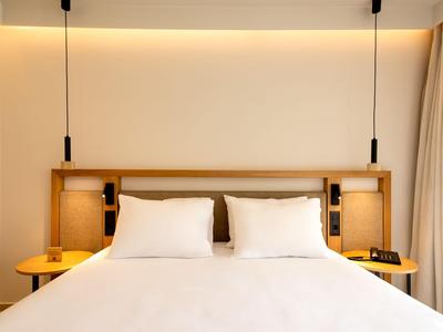 Modernes Hotelzimmer mit breitem Bett, Holzkopfteil und sanfter Beleuchtung.