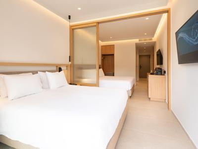 Modern eingerichtetes Hotelzimmer mit zwei Doppelbetten, Fernseher und Beleuchtung.