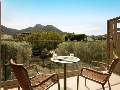 Balkon mit zwei Stühlen und Tisch, Blick auf Berge und grüne Landschaft bei klarem Himmel.