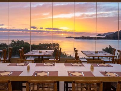 Essbereich mit Holzstühlen und Tischen mit Blick auf Meer und Sonnenuntergang.