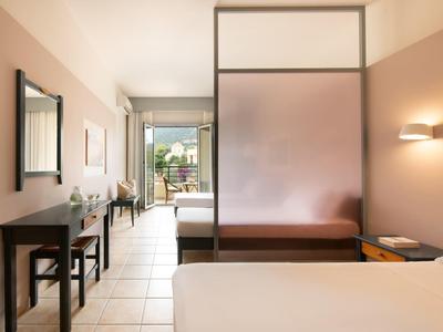 Hell eingerichtetes Hotelzimmer mit Doppelbett und halbtransparentem Raumteiler.