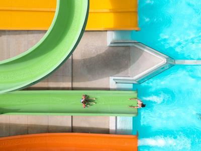 Blick von oben auf Wasserrutschen mit Menschen, die ins blaue Wasser gleiten.