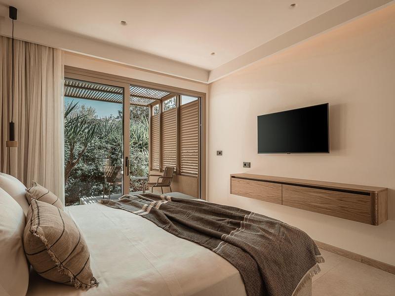 Modernes Hotelzimmer mit Doppelbett, Wandfernseher und Blick auf Terrasse mit Pflanzen.