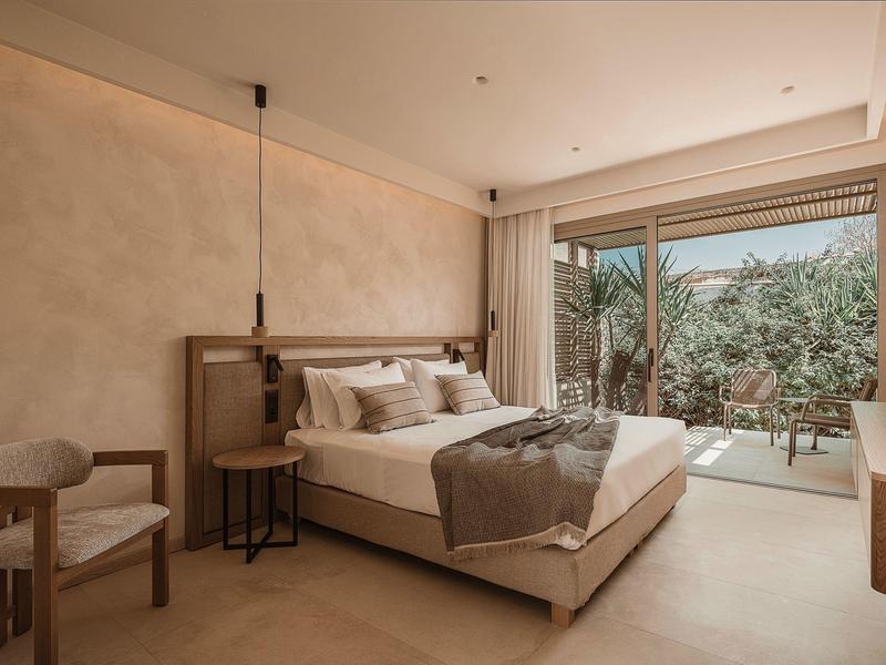 Modernes Hotelzimmer mit Doppelbett, Sitzbereich und großer Glastür zur Terrasse mit Pflanzen.