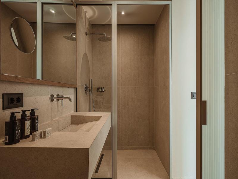 Modernes Badezimmer mit Waschbecken, Spiegel und Glastür zur Dusche in neutralen Farbtönen.