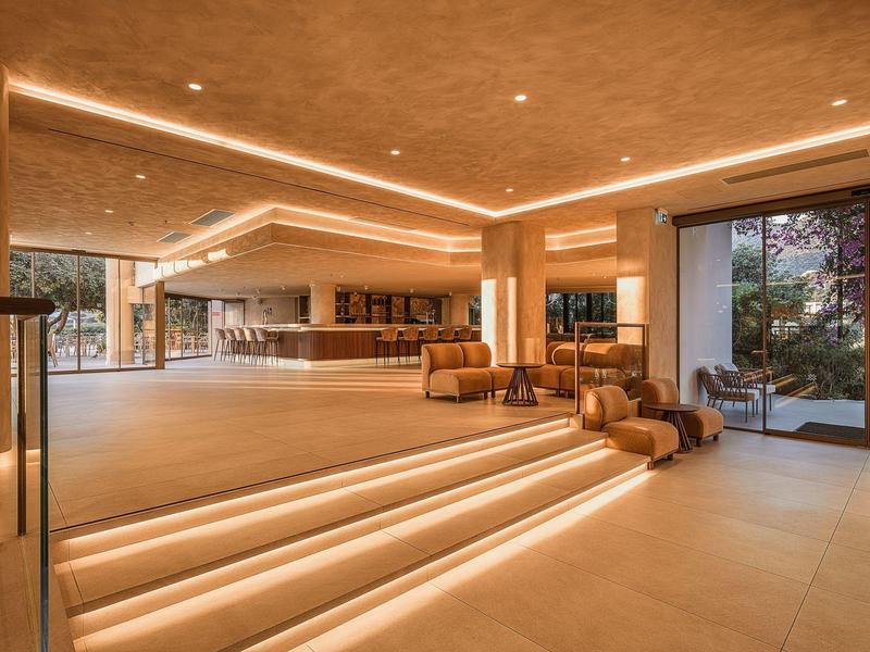 Moderner Hotel-Loungebereich mit bequemen Sesseln, beleuchteten Stufen und großem Fenster mit Blick auf die Natur.