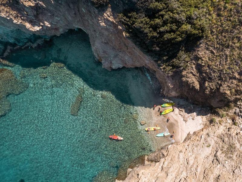 Luftaufnahme einer felsigen Küste mit klar blauem Wasser und Kajakfahrern nahe dem Strand