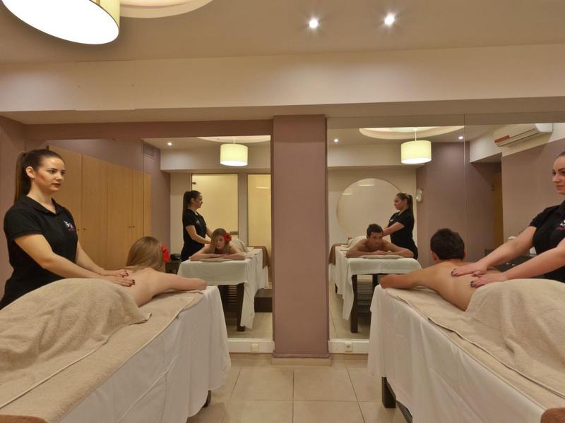 Zwei Frauen massieren Männer in einem ruhigen Spa-Raum mit warmem Licht.