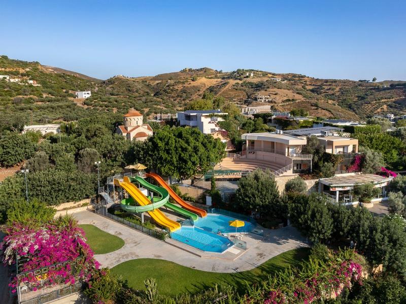 Freizeitpark mit Wasserrutschen und Schwimmbecken, umgeben von grünen Hügeln und Gebäuden.
