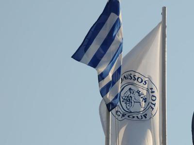 White flag with logo and blue-white striped flag against clear sky