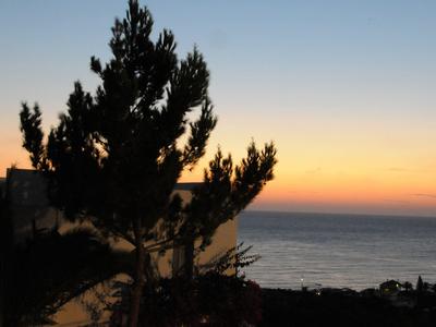 Sunset over the sea with silhouettes of trees and buildings in the foreground