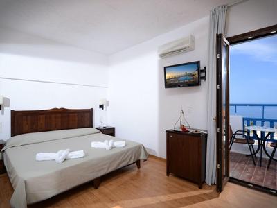 Bright hotel room with double bed, air conditioning, and balcony with sea view at dusk.