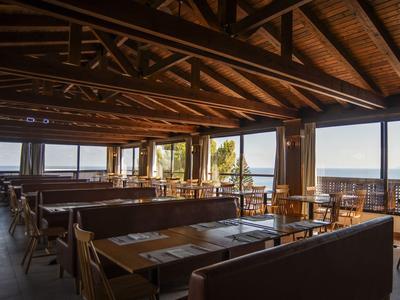 Restaurante con techo de madera y grandes ventanas con vistas al mar en la costa.