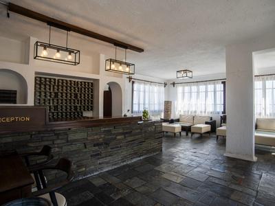 Empfangsbereich eines Hotels mit Steinrezeption und Sitzgelegenheiten in hellem Raum.