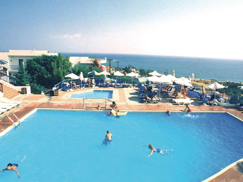 Large outdoor pool with swimmers, lounge chairs, and sea view in the background.