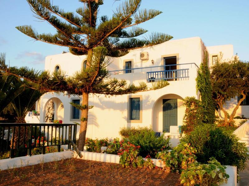 White holiday house with balcony and blue shutters in sunny setting with trees
