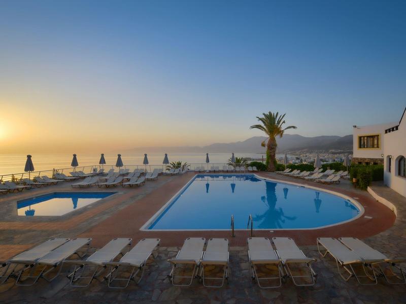 Hotel pool with loungers and sea view at sunset.