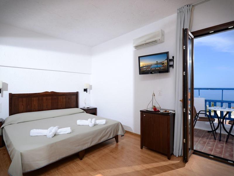 Bright hotel room with double bed, air conditioning, and balcony with sea view at dusk.