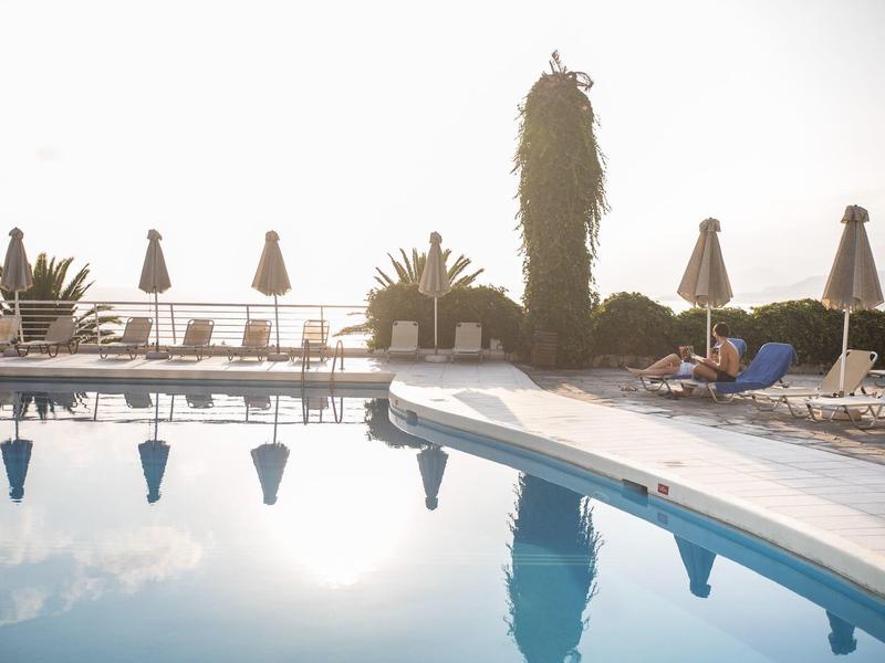 Empty pool with sun umbrellas and lounge chairs in morning light.