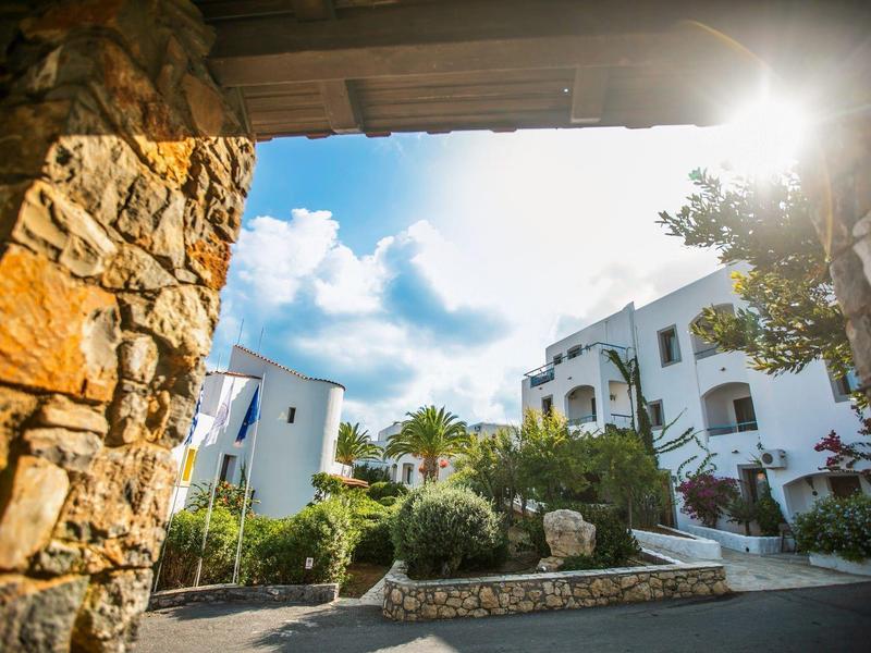Sunny view of a Mediterranean hotel with white buildings and a stone archway