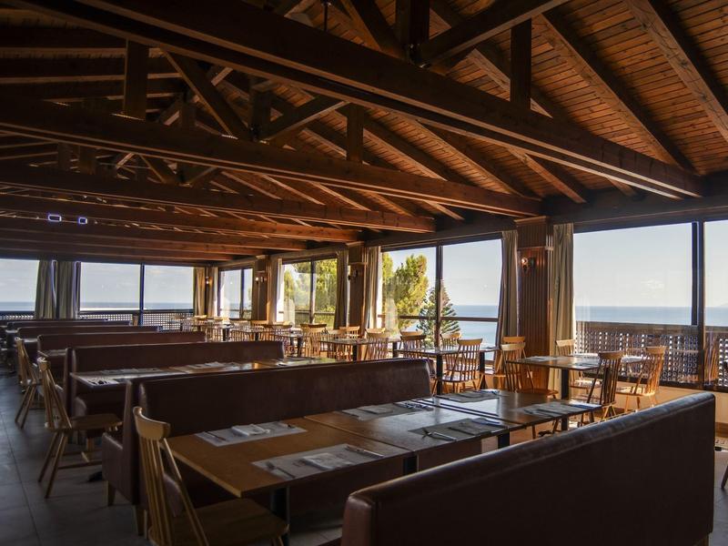 Restaurant with wooden ceiling and large windows overlooking the sea.