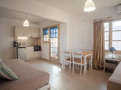 Sala luminosa con sofá, mesa de comedor, kitchenette y ventanas grandes con cortinas.